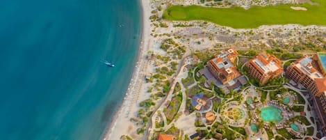 Eine Vogelperspektive eines Küstenresorts mit mehreren Gebäuden, einem Strand und einem Golfplatz.
