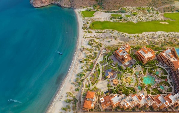 An aerial view of a coastal resort with multiple buildings, a beach, and a golf course.