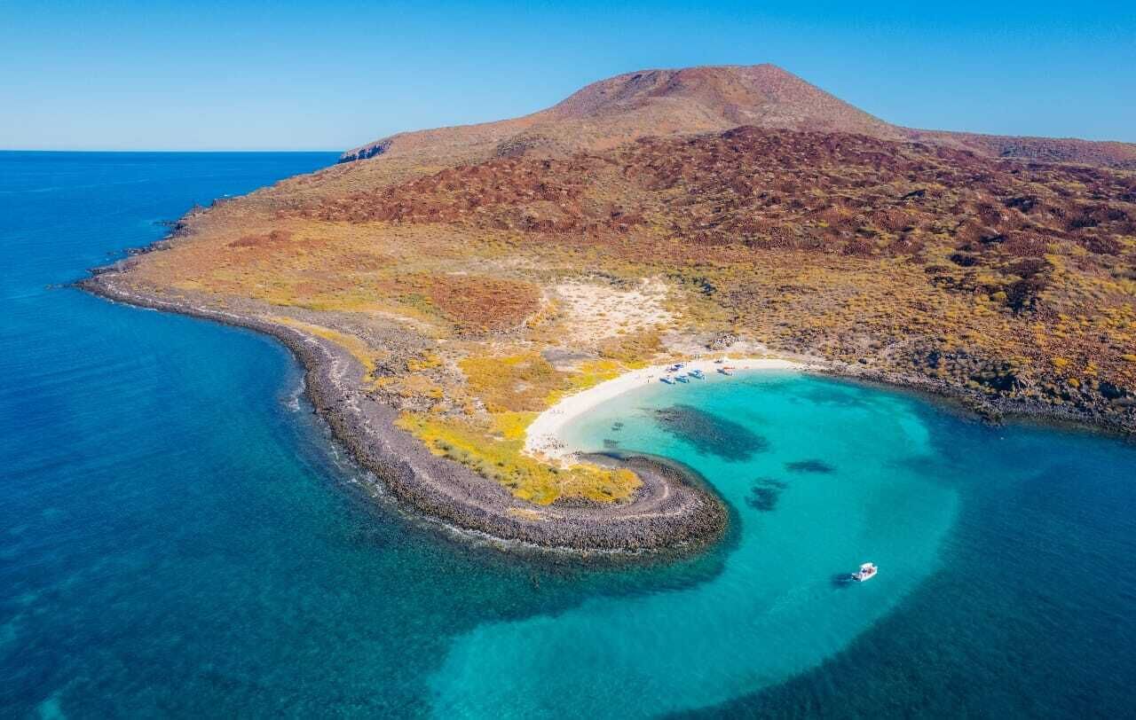 An aerial view of a coastal landscape with a beach, clear waters, and a mountain in the background.