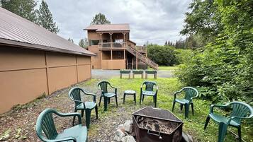 A building with a wooden exterior and a balcony, surrounded by green chairs and a fire pit.