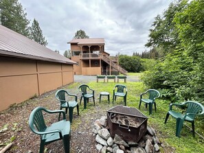 A building with a wooden exterior and a balcony, surrounded by green chairs and a fire pit.