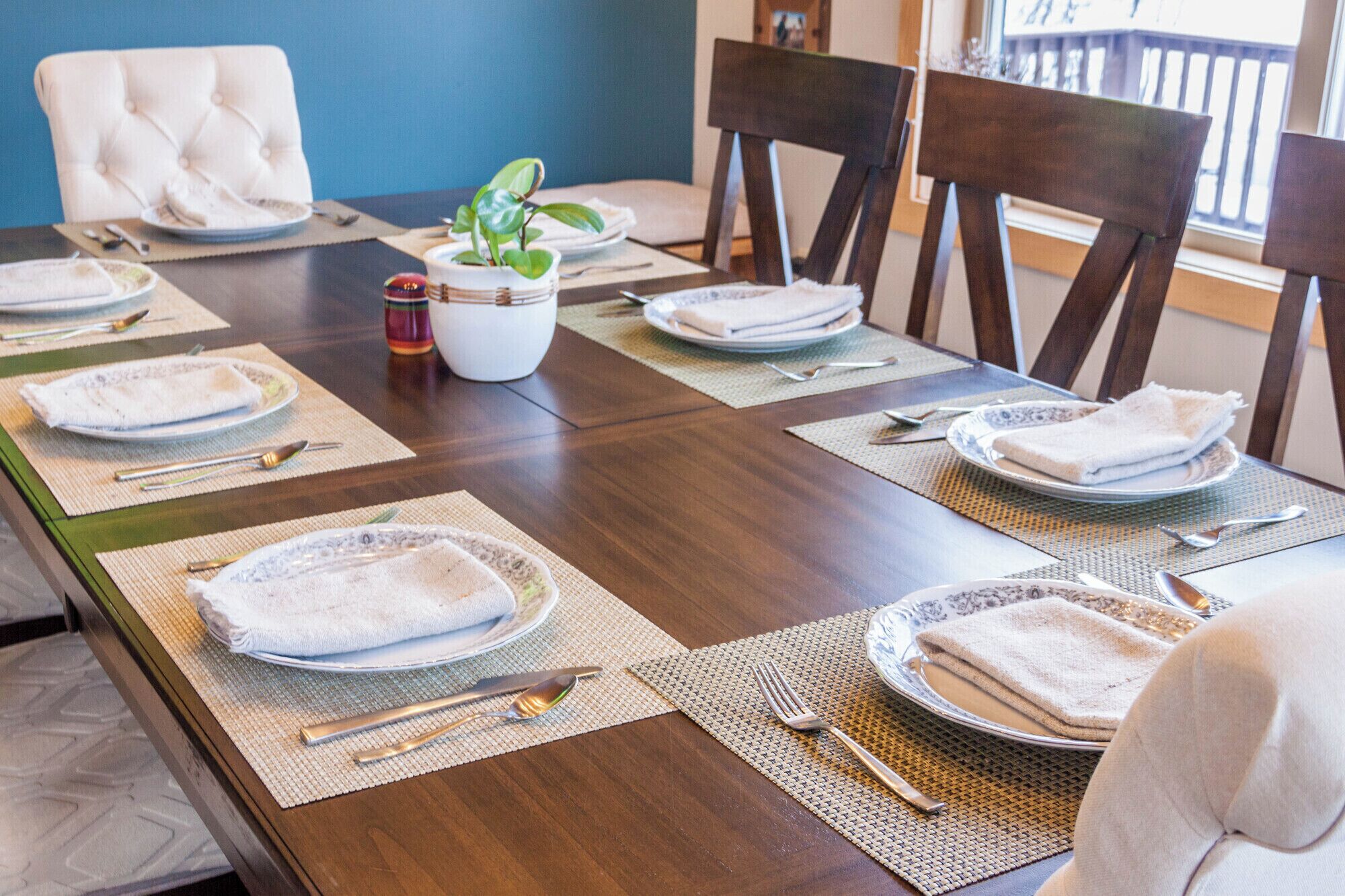 A dining table set with plates, cutlery, and napkins, surrounded by chairs.