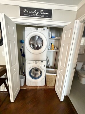 A laundry room with a sign above a stacked washer and dryer, a mop, and cleaning supplies. - Cozy Lake Escape on Weiss Lake (Cedar Bluff)