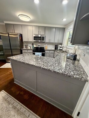 A modern kitchen with granite countertops, stainless steel appliances, and recessed ceiling lighting. - Cozy Lake Escape on Weiss Lake (Cedar Bluff)
