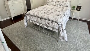 Ein Schlafzimmer mit Bett, Deckenventilator, Fernseher, Kommode, Nachttisch und einer Wandtafel.