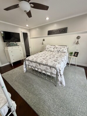 A bedroom with a bed, a ceiling fan, a television, a dresser, a bedside table, and a wall sign. - Cozy Lake Escape on Weiss Lake (Cedar Bluff)