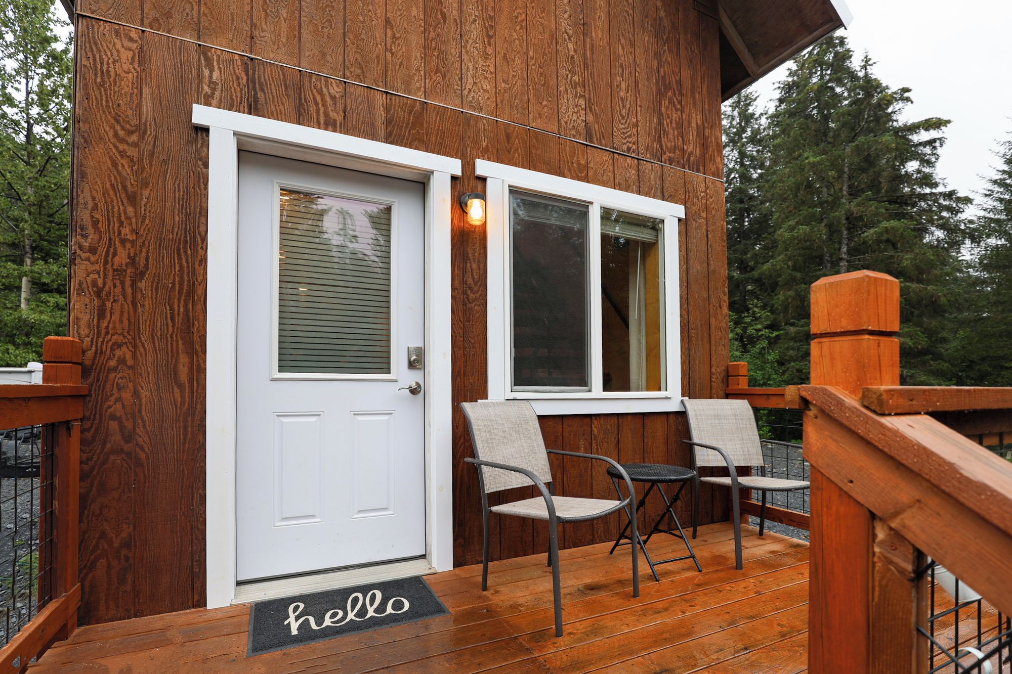 A wooden deck with a white door, two windows, and a 'hello' mat.