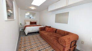 A modern bedroom with a bed, a sofa, a mirror, and a ceiling light. - Luxury Condo with Walk-In Elevator and Patios (Los Angeles)