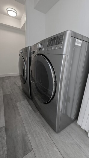 A modern, stainless steel front-loading washer and dryer unit in a clean, minimalistic laundry room with a wooden floor. - Luxury Condo with Walk-In Elevator and Patios (Los Angeles)