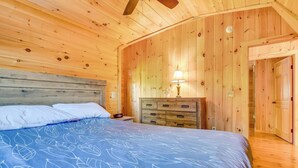 Ein Schlafzimmer in einer Holzhütte mit einem Bett, einem Nachttisch, einer Kommode und einer Tür zu einem anderen Raum.