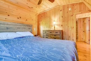 Ein Schlafzimmer in einer Holzhütte mit einem Bett, einem Nachttisch, einer Kommode und einer Tür zu einem anderen Raum.