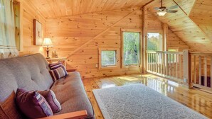 Ein Holzblockhaus im Inneren mit einer Couch, einem kleinen Tisch, einem Teleskop und einem Balkon.