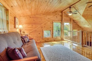 Ein Holzblockhaus im Inneren mit einer Couch, einem kleinen Tisch, einem Teleskop und einem Balkon.