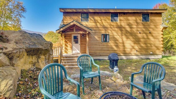 Eine Holzhütte mit Veranda, zwei Stühlen und einem Grill.