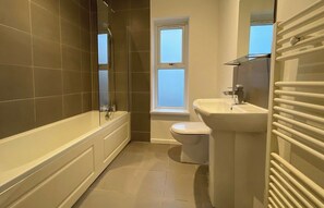 Een badkamer met een badkuip, toilet en een raam.