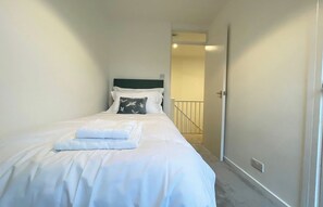 Une chambre d’hôtel avec un lit simple, du linge de lit blanc, un oreiller orné d’un motif d’oiseau et une serviette soigneusement pliée.