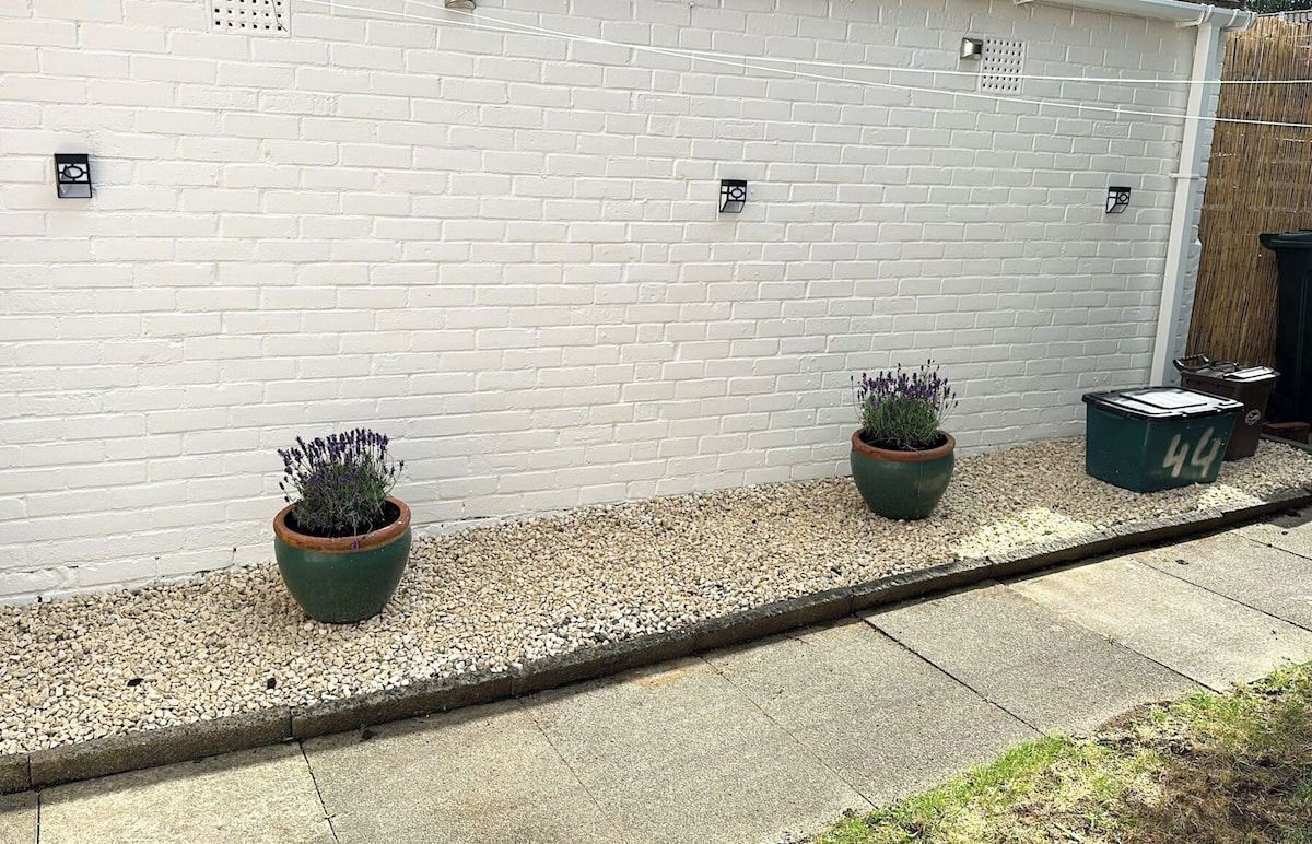 A white brick wall with two potted plants and a trash bin.