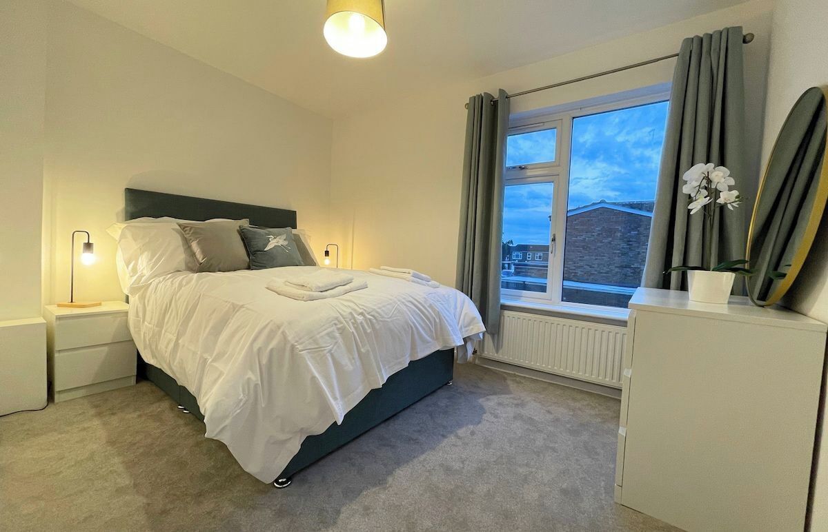 Une chambre à coucher avec un lit, des lampes de chevet, une fenêtre avec des rideaux et un radiateur.
