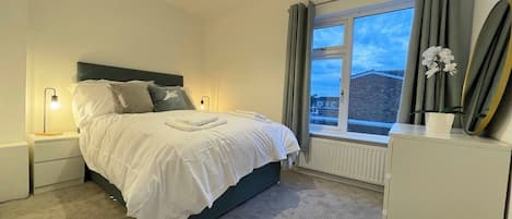 A bedroom with a bed, bedside lamps, a window with curtains, and a radiator.