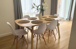 Een eethoek met een ronde tafel, zes stoelen en een vaas met bloemen.