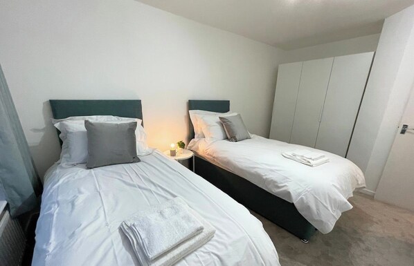 Une chambre d’hôtel avec deux lits simples, une table de chevet avec une lampe et une armoire.