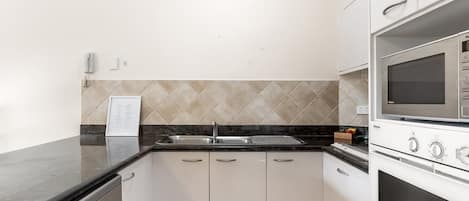 A kitchen with white cabinets, a black countertop, a stainless steel sink, and a built-in microwave oven.