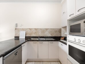 Een keuken met witte kastjes, een zwart aanrecht, een roestvrijstalen spoelbak en een ingebouwde magnetron.
