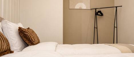 Un dormitorio con cama, almohadas, una obra de arte en la pared y un perchero negro sobre un soporte.