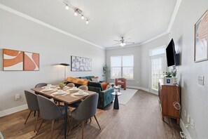Un salon moderne comprenant un coin repas, un ventilateur de plafond et un téléviseur à écran plat fixé au mur.