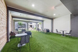 Un espace intérieur doté d’un revêtement de sol en gazon synthétique, d’espaces aménagés pour s’asseoir et d’une vue sur un bâtiment adjacent.