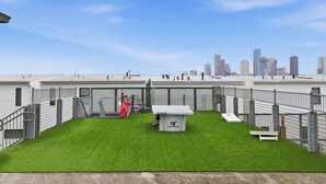 Eine Dachterrasse mit Rasen, einem kleinen Gebäude und einer Stadtkulisse im Hintergrund.