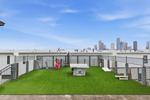 Eine Dachterrasse mit Rasen, einem kleinen Gebäude und einer Stadtkulisse im Hintergrund.