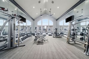 Ein Fitnessstudio mit verschiedenen Trainingsgeräten, großen Fenstern und hoher Decke.