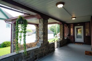 A covered porch with stone pillars, a hanging planter, and a wooden door.