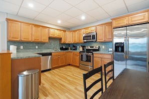 A modern kitchen with wooden cabinets, stainless steel appliances, a granite countertop, and a wooden floor.