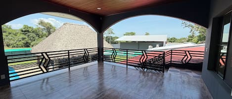 A spacious balcony with a wooden ceiling and a view of a building with a thatched roof.