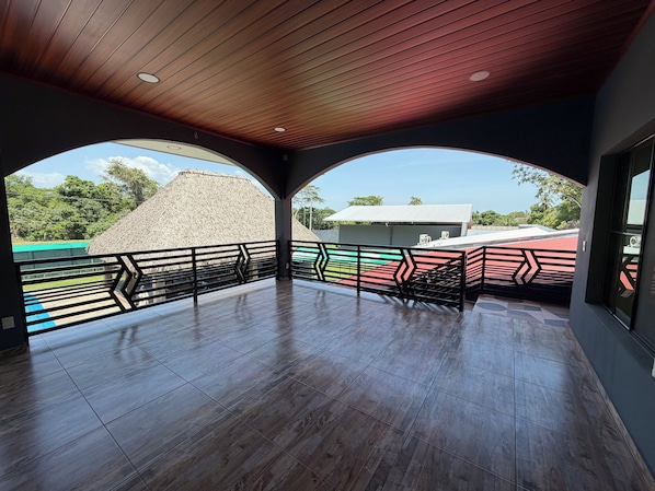 A spacious balcony with a wooden ceiling and a view of a building with a thatched roof.