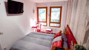Un dormitorio con cama, escritorio, silla y televisor en la pared.