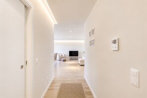 A modern hallway leading to a living area with a flat-screen TV, a sofa, and a wall-mounted thermostat. - Spacious 2-Suite Flat with Balconies | Portimão (Portimão)