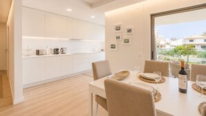 Una cocina moderna con armarios blancos, un comedor con una mesa dispuesta para dos personas y vistas al exterior.