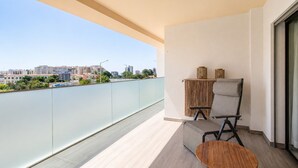 Un balcón con vistas a un paisaje urbano, una silla, una mesita y un panel decorativo en la pared.