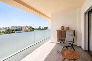 Ein Balkon mit Blick auf eine Stadtlandschaft, ein Sessel, ein kleiner Tisch und ein dekoratives Wandpaneel.