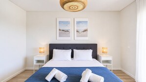 Habitación de hotel con una cama, dos lámparas de noche, un ventanal grande y dos cuadros en la pared.
