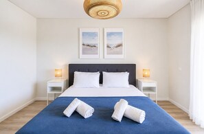 Ein Hotelzimmer mit einem Bett, zwei Nachttischlampen, einem großen Fenster und zwei gerahmten Bildern an der Wand.
