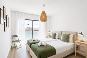 Ett hotellrum med två sängar, utsikt över staden, en stol och en hängande lampa.