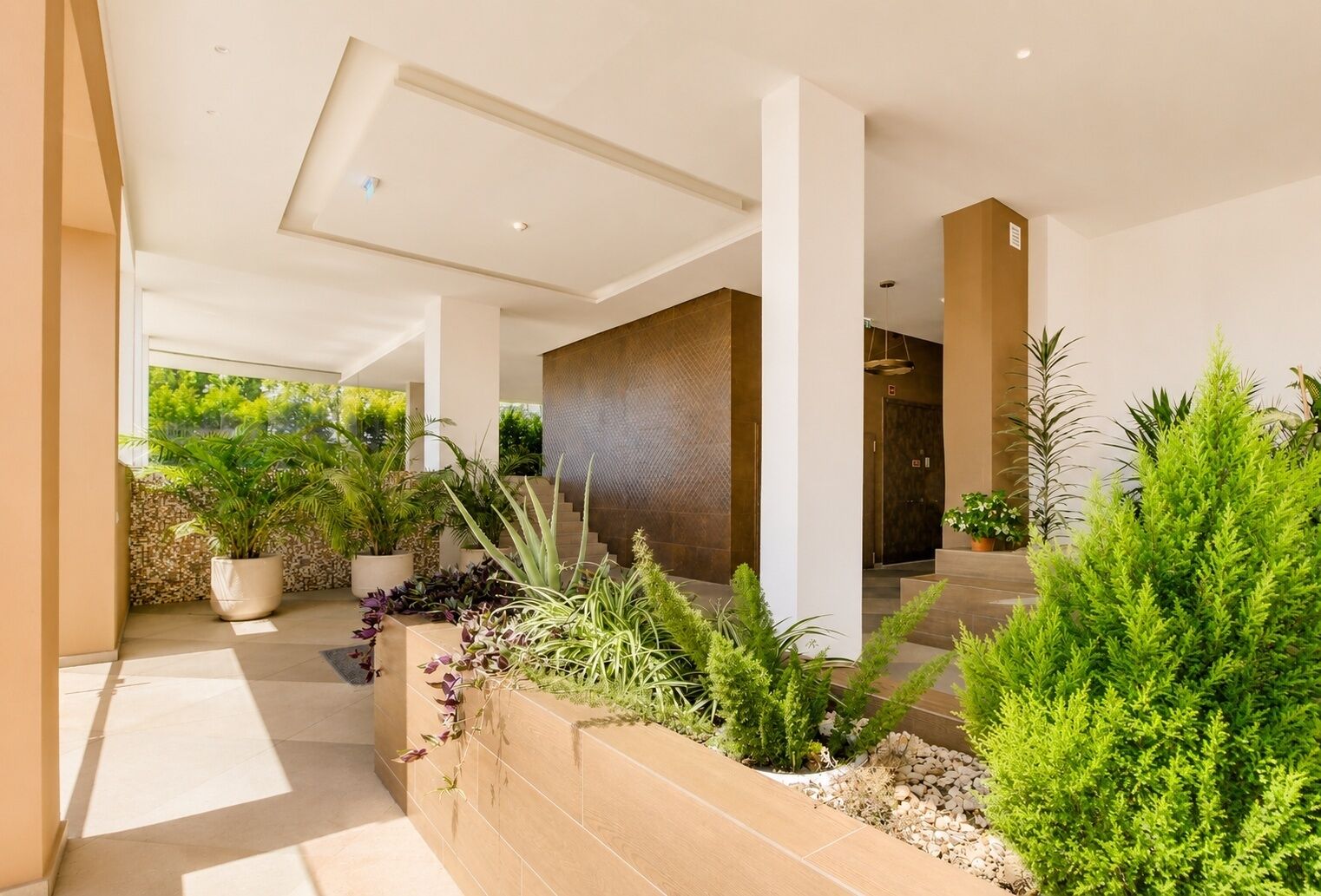 A modern building with a covered outdoor area, potted plants, and a staircase leading to an elevator.