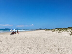 Ein Strand mit blauem Himmel, wenigen Personen und einem blauen Sonnenschirm.