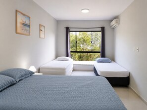 A room with two single beds, a large bed, a window with curtains, and a ceiling light. - CasAmar a 50m Praia Pontal do Peró - Cabo Frio/RJ (Cabo Frio)