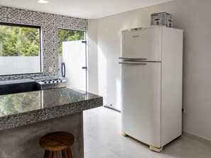 A kitchen with a white refrigerator, a stove, and a window with a view of greenery. - CasAmar a 50m Praia Pontal do Peró - Cabo Frio/RJ (Cabo Frio)