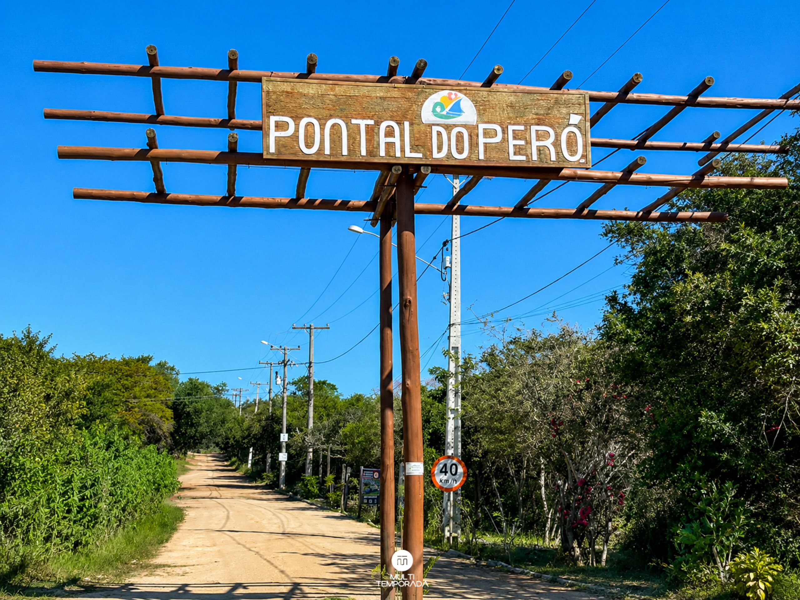 Une enseigne en bois portant l’inscription « PONTAL DO PERÓ » et un logo, fixée sur une structure en bois avec des poutres horizontales.